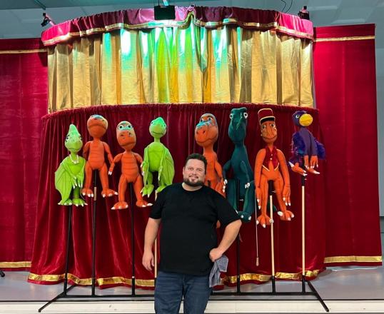 A man standing in front of puppets. 